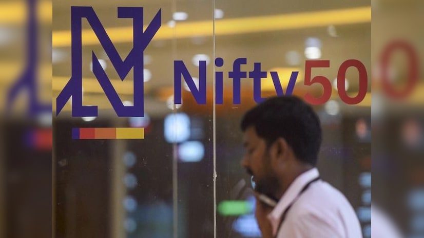 A man talks on phone at the National Stock Exchange as its new logo for for the benchmark Nifty50 is seen on a glass-wall, in Mumbai